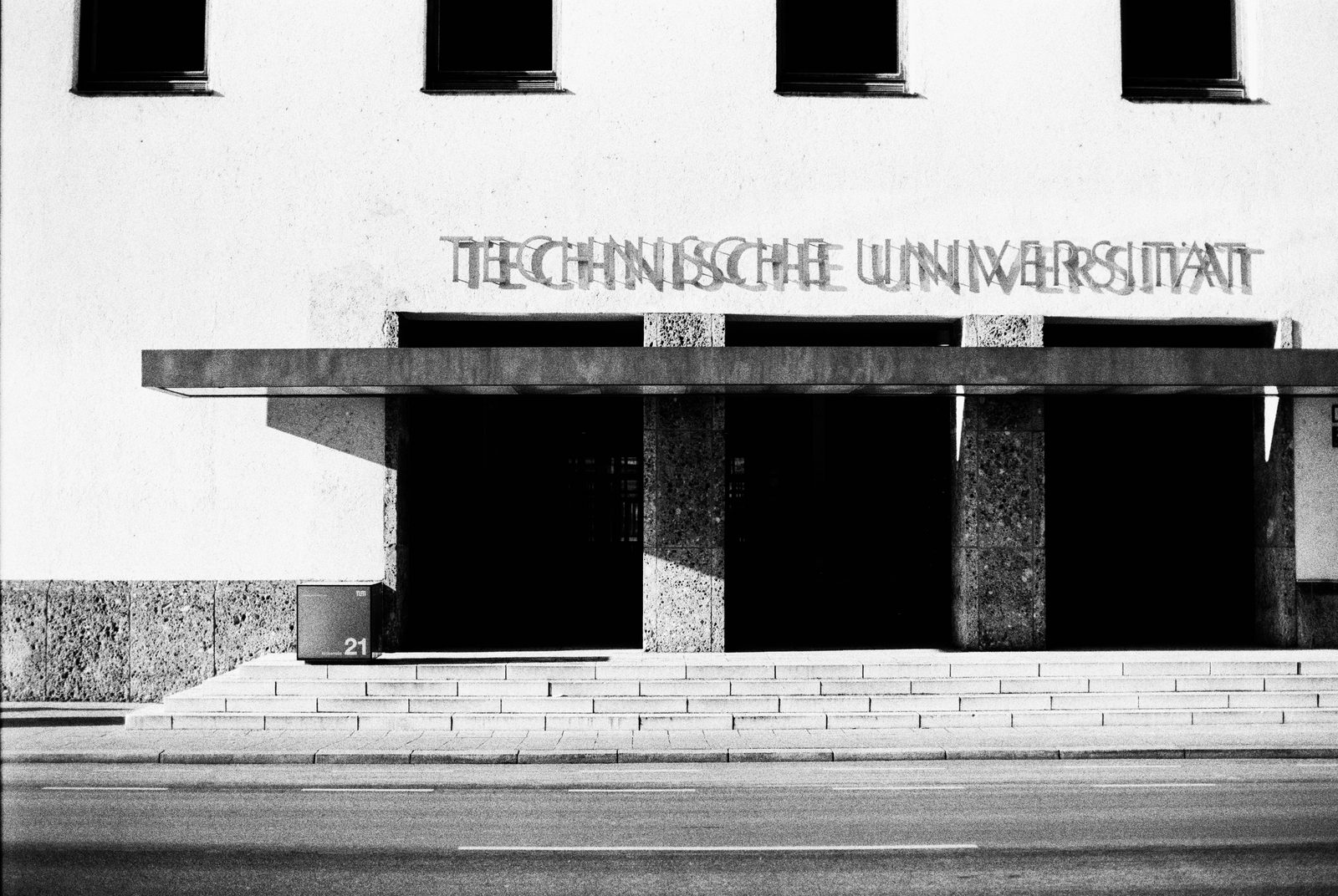 Eingang Technische Universität München, Arcisstraße 21: frontaler Schwarzweiß-Blick auf die rhythmische Pfeilerreihe des Vordachs und den Schriftzug ‚Technische Universität'.